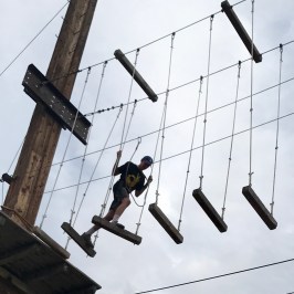 boy running across logs on the high ropes course